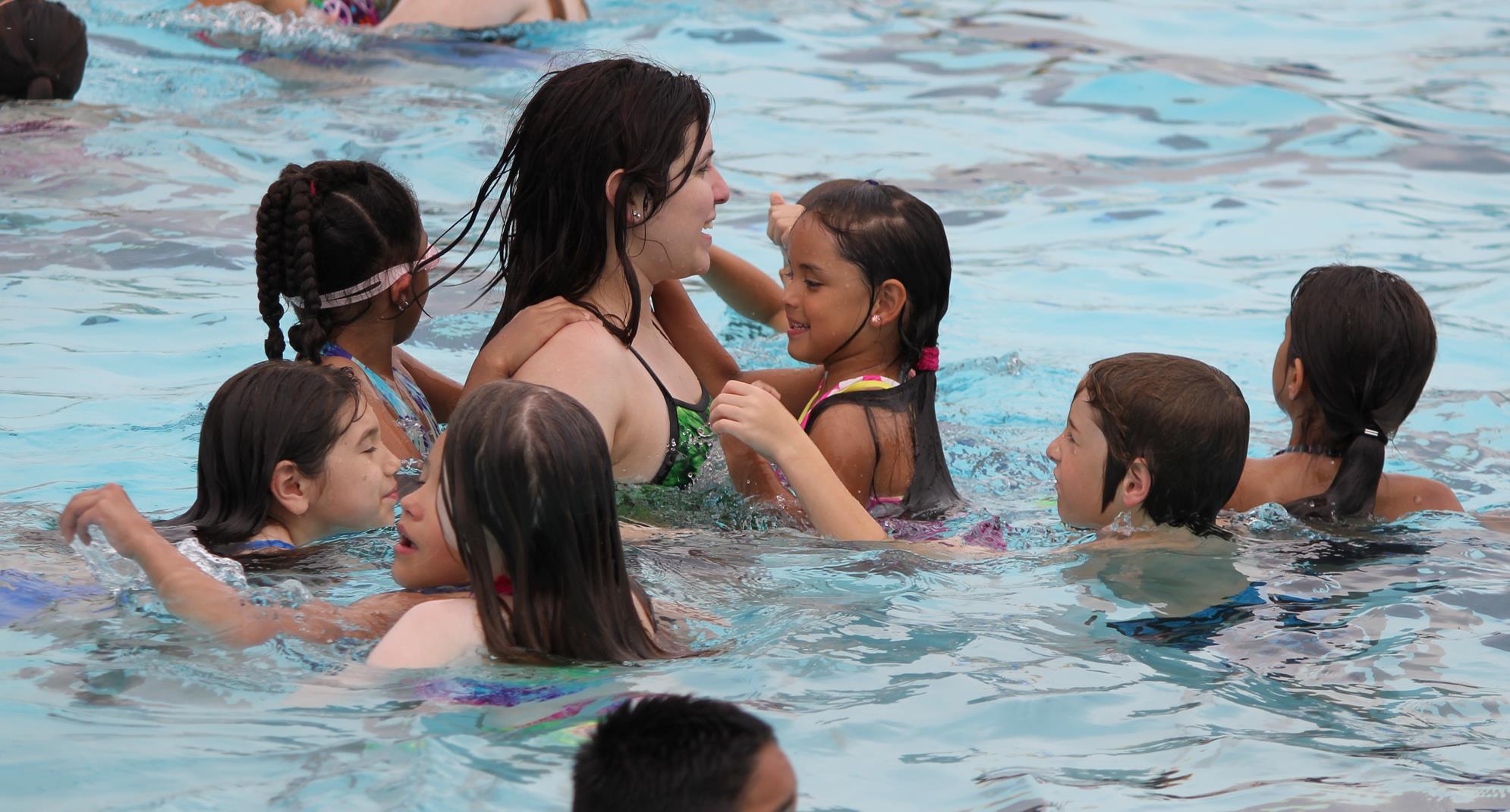 Adult in pool playing with group of kids
