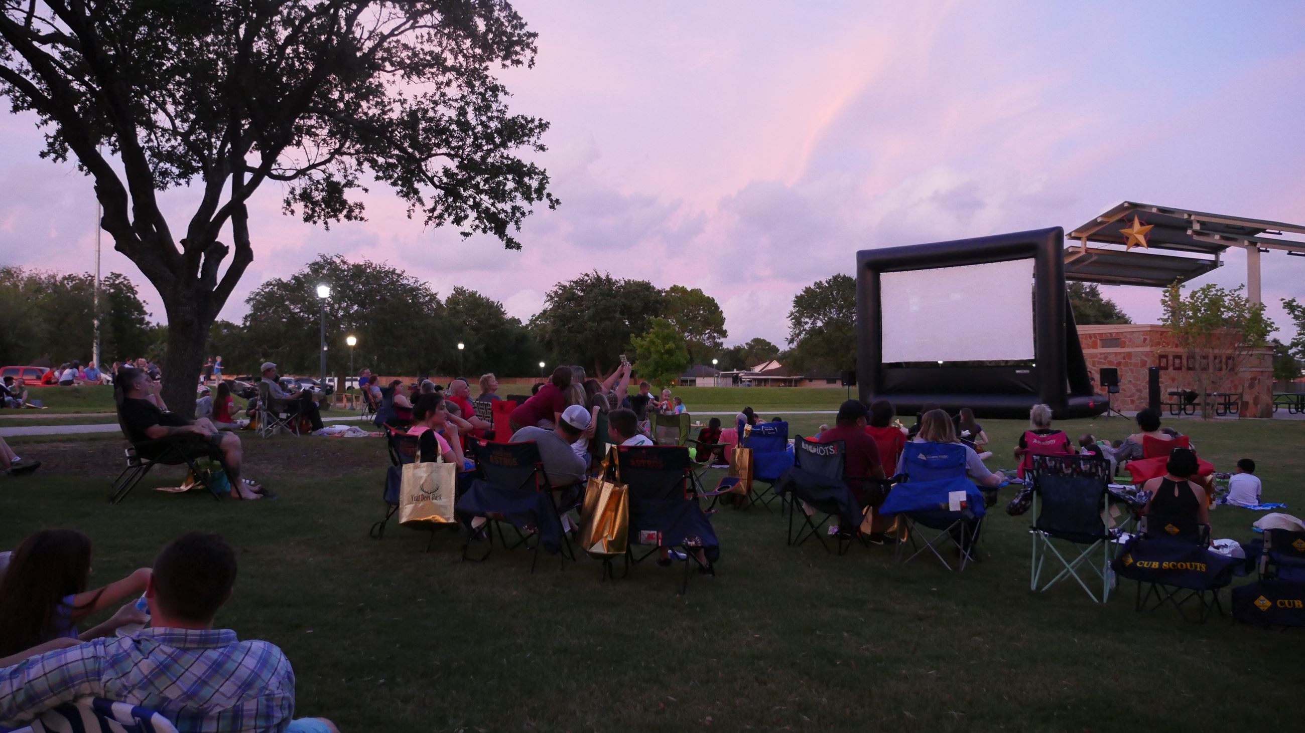 Movie screen with sunset behind it - families sitting on blankets outside watching movie 